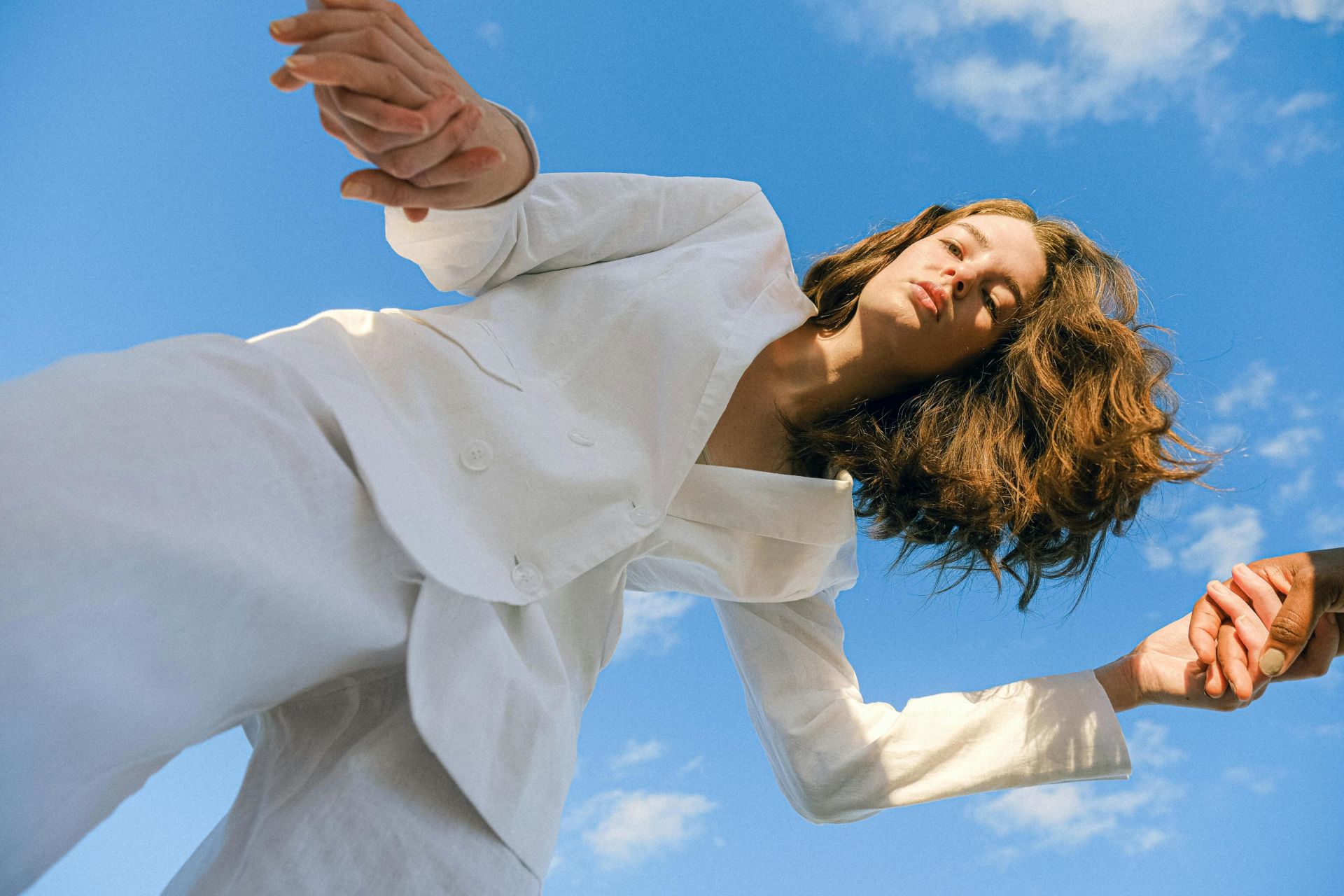 A woman in a white suit poses gracefully against a vibrant blue sky.