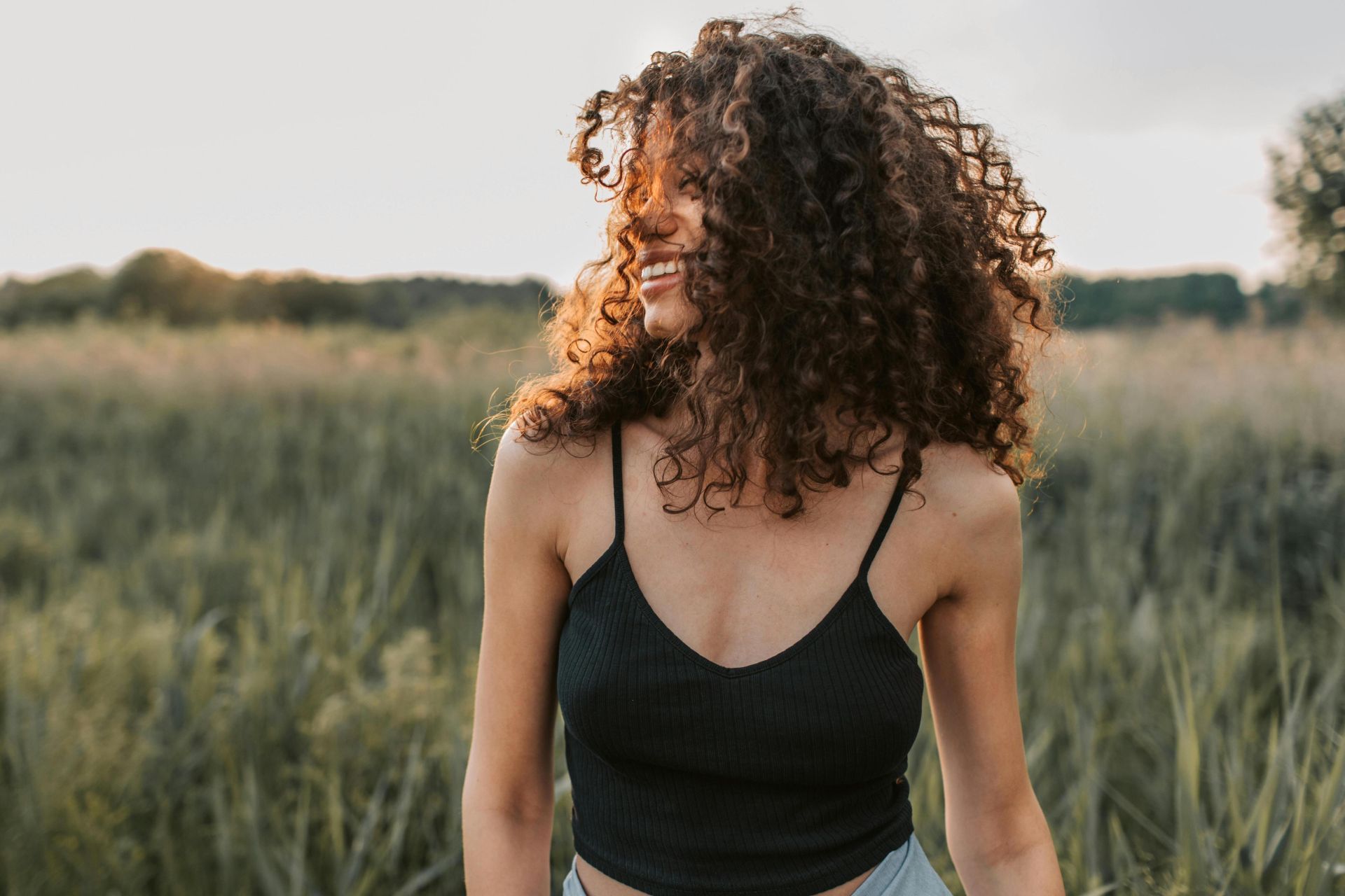 A cheerful woman in casual attire enjoying a sunny day outdoors with natural curly hair.
