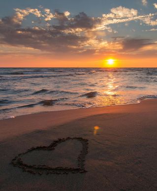 Beautiful sunset over ocean with a heart shape in the sand, perfect for romantic themes.