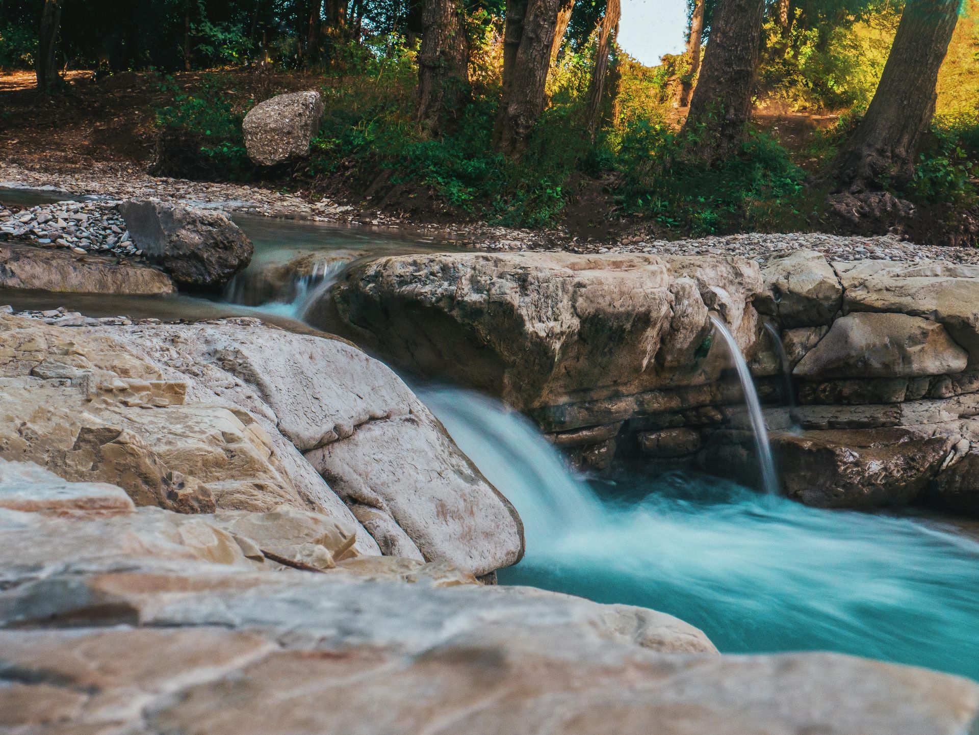 A tranquil waterfall flows over rocks in a lush forest setting, capturing nature's beauty.