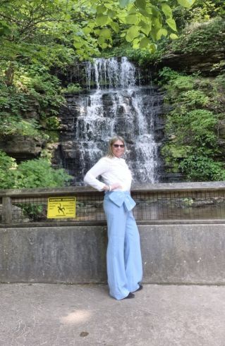 A thoughtful woman with afro hair in a gray blazer poses indoors, conveying a sense of introspection.