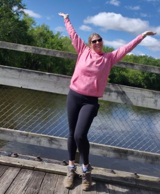 A woman in a pink dress raises her hands in prayer outdoors during twilight, expressing serenity and spirituality.